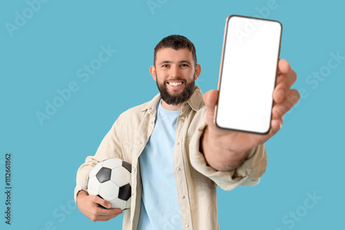 Handsome young happy man with soccer ball and mobile phone on blue background. Concept of sports bet photo