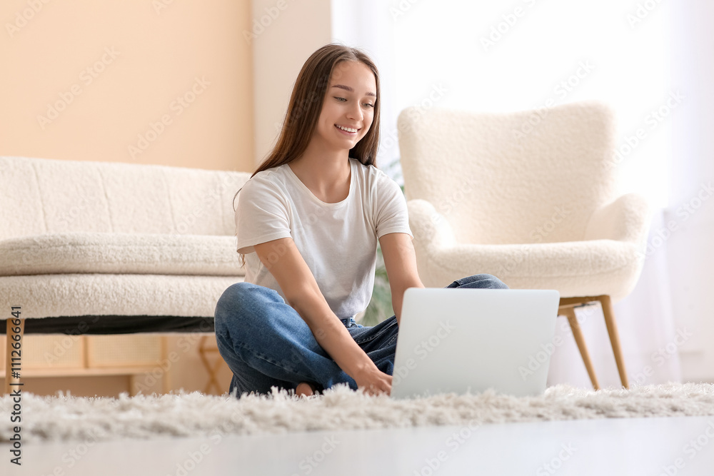 Young happy woman sitting on floor and using laptop near sofa in living room Young happy woman sitting on floor and using laptop near sofa in living room