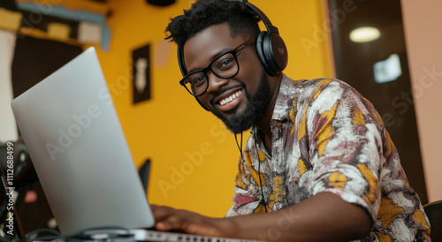 Homem africano usando fones de ouvido e trabalhando com laptop, sorrindo e olhando para a câmera. photo