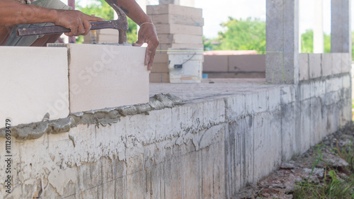 Workers Masonry are laying brick walls on the building structure along the house pillars.