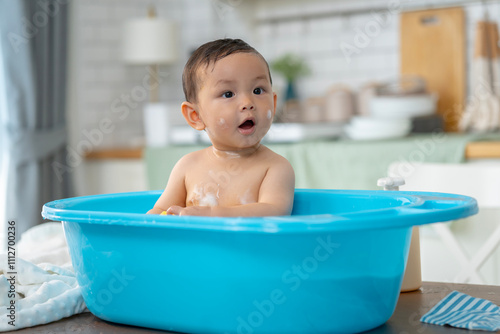 Asian baby taking a bath in a blue tub at home.