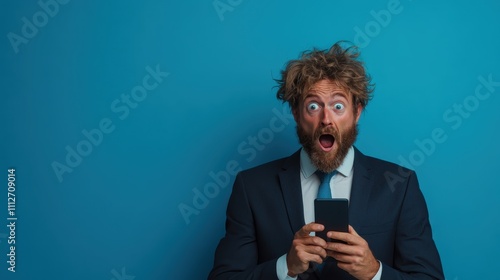 A surprised businessman with wild hair and a suit, holding a smartphone against a blue background, reacting with shock or excitement to unexpected news. photo