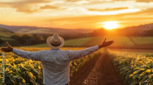 The image showcases a person in a straw hat enjoying a picturesque sunset over lush green fields, embodying freedom and contentment in a rural setting. photo