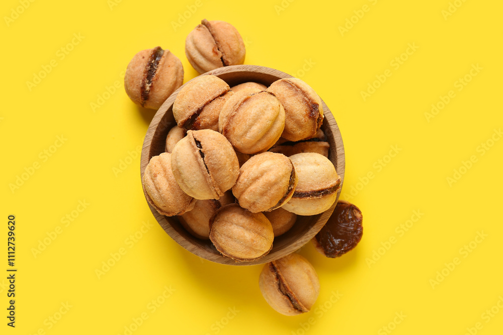 Wooden bowl with sweet walnut shaped cookies with boiled condensed milk on yellow background Wooden bowl with sweet walnut shaped cookies with boiled condensed milk on yellow background