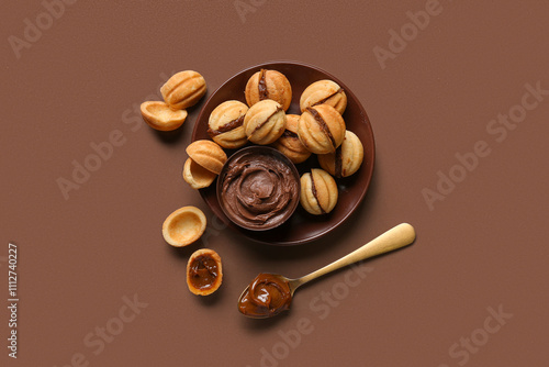 Bowl of sweet walnut shaped cookies with boiled condensed milk on brown background photo