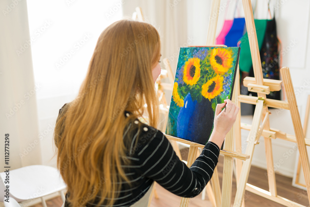 Woman artist painting still life of sunflowers in blue vase on canvas using paintbrush in art studio Woman artist painting still life of sunflowers in blue vase on canvas using paintbrush in art studio