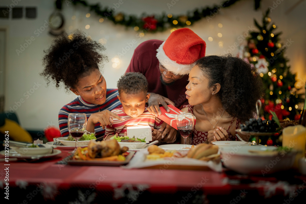 A joyful family gathers around the dinner table celebrating Christmas. The father, dressed in a Santa hat, gives a gift to the child, while everyone smiles with warmth and festive decorations. A joyful family gathers around the dinner table celebrating Christmas. The father, dressed in a Santa hat, gives a gift to the child, while everyone smiles with warmth and festive decorations.