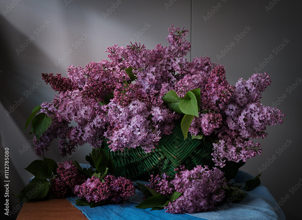 A beautiful arrangement of lilac flowers is displayed in a white vase on a table. The flowers are in full bloom and their vibrant color creates a sense of freshness and vitality.