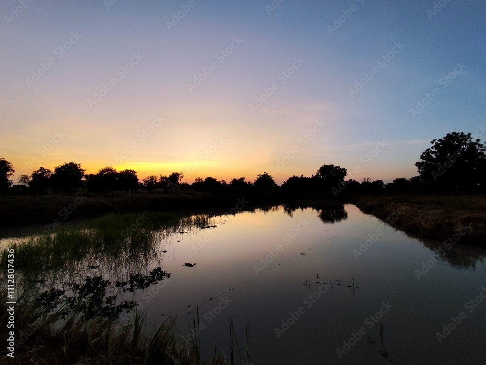 A beautiful sunset painted the sky orange and reflected on a tranquil lake surrounded by lush green trees. A beautiful sunset painted the sky orange and reflected on a tranquil lake surrounded by lush green trees.