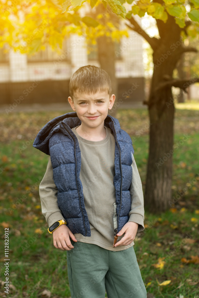 Child wearing a blue quilted vest and beige shirt, standing in a park with autumn foliage. Perfect for themes of outdoor activities, children’s fashion, and seasonal changes Child wearing a blue quilted vest and beige shirt, standing in a park with autumn foliage. Perfect for themes of outdoor activities, children’s fashion, and seasonal changes