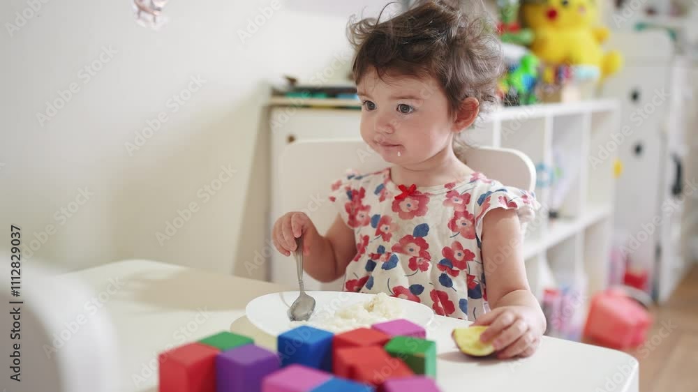 the girl eats at the table. happy family child dream concept. girl sits indoors at a white table and eats food with her hands near small toy cubes food. child's lifestyle the girl eats at the table. happy family child dream concept. girl sits indoors at a white table and eats food with her hands near small toy cubes food. child's lifestyle