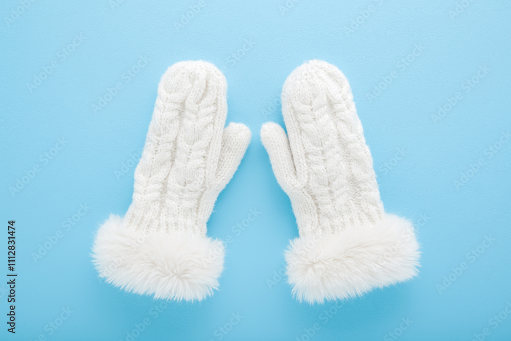 White soft beautiful knitted warm winter female mittens with fluffy fur on light blue table background. Pastel color. Closeup. Top down view. White soft beautiful knitted warm winter female mittens with fluffy fur on light blue table background. Pastel color. Closeup. Top down view.