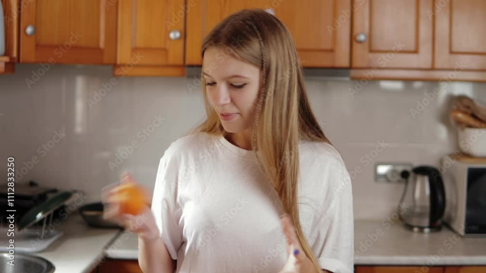 Girl in a white t-shirt juggles oranges in a bright kitchen. Cheerful and focused, she displays her skill while enjoying a playful moment in a lively home environment Girl in a white t-shirt juggles oranges in a bright kitchen. Cheerful and focused, she displays her skill while enjoying a playful moment in a lively home environment