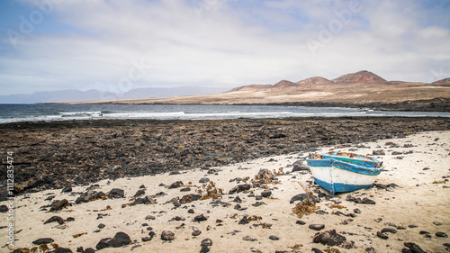 bateau en bois bleu et blanc échoué sur une plage de sable avec des montagne en arrière plan