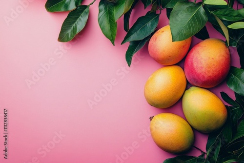 Freshly picked ripe mangoes arranged with vibrant green leaves on a pink back...
