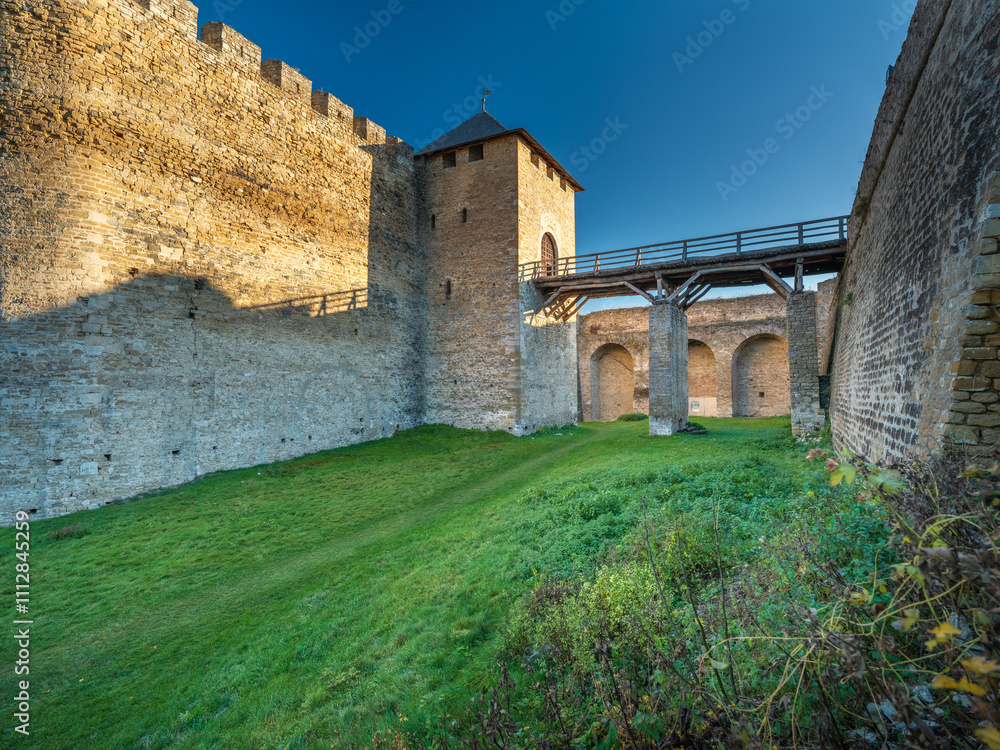 view to yard of fortress with bridge between walls and green grass under blue sky view to yard of fortress with bridge between walls and green grass under blue sky