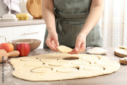 Woman making pirozhki (stuffed pastry pies) at wooden table indoors, closeup photo