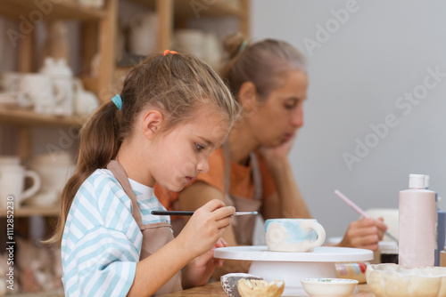 mother and child daughter paint the clay mugs they made crafts pottery school. A professional potter teaching and coaching kid making a pottery in the workshop. 
