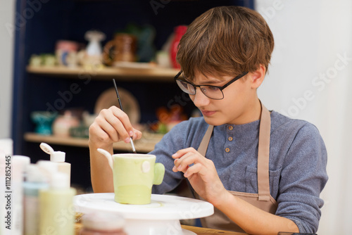 teenager boy paint the clay mugs they made in pottery school.  Children arts a crafts class in workshop. Kid sculpts clay crafts pottery school.