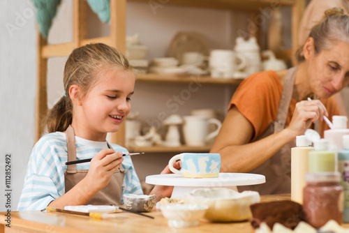 mother and child daughter paint the clay mugs they made crafts pottery school. A professional potter teaching and coaching kid making a pottery in the workshop. 
