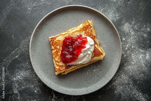 Delicious pancake topped with cream and fruit preserves on a dark plate with ...