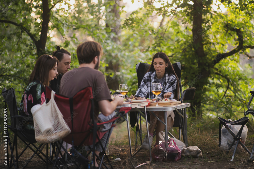 group of four friends enjoys a picnic meal outdoors under a large tree. They sit at a folding table, surrounded by nature group of four friends enjoys a picnic meal outdoors under a large tree. They sit at a folding table, surrounded by nature