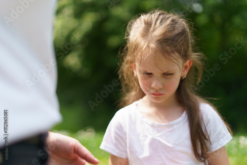 Little sad girl in a T-shirt next to her mother in a summer park. Concept of difficult childhood