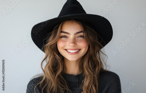 Smiling young woman with long hair and a large black hat posing against a lig...