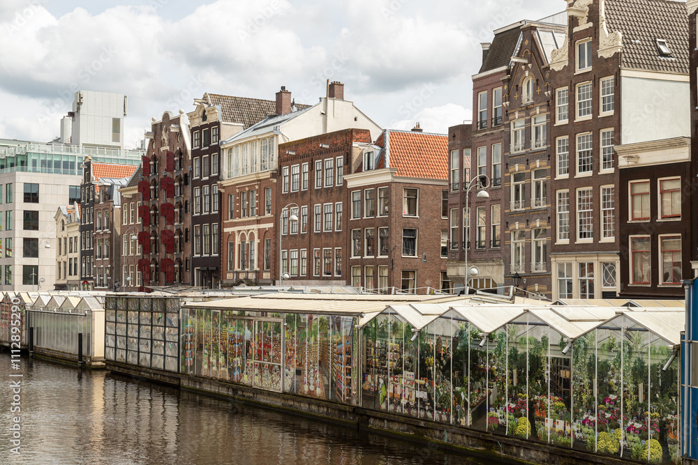 Amsterdam floating flower market and tall narrow historic canal houses along the Singel in the center of the capital. Amsterdam floating flower market and tall narrow historic canal houses along the Singel in the center of the capital.