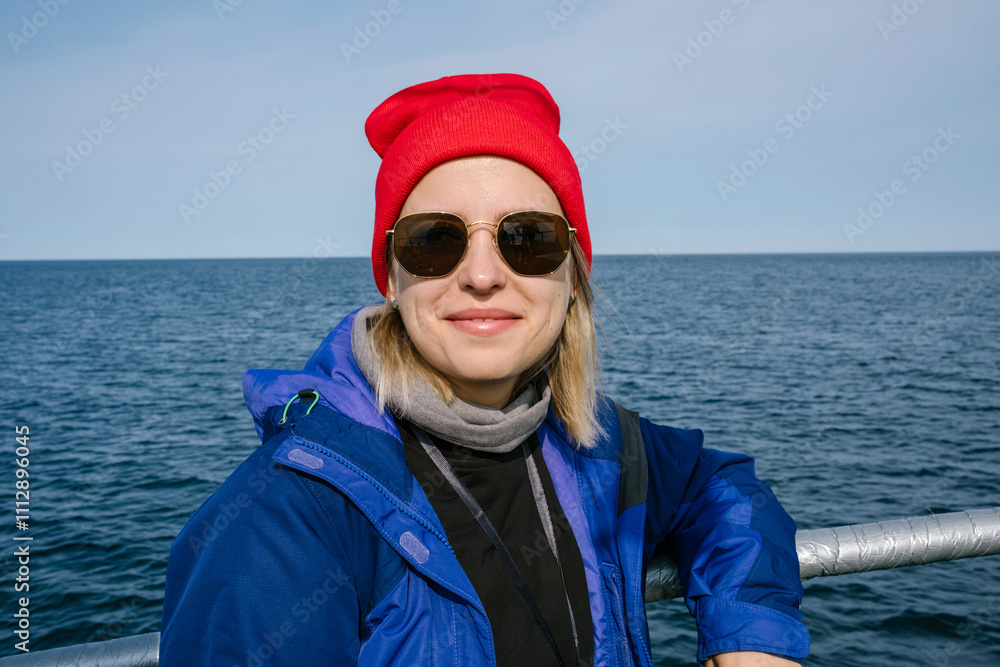 A Woman Smiles While Wearing Sunglasses and a Red Beanie in the Sea A Woman Smiles While Wearing Sunglasses and a Red Beanie in the Sea