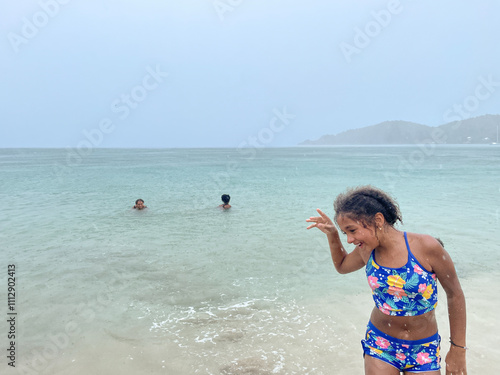 Preteen standing in the clear ocean water on a rainy  beach day photo