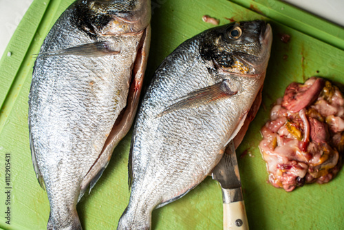 Fotografia Gutted dorado fish with knife and giblets on a green cutting board background