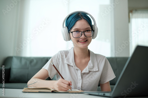 A girl wearing blue hair and glasses is sitting at a table with a laptop