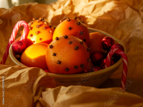 Cristmas decorations. Christmas crafts. Oranges decorated with carnation, laying in a porcelain bowl with red tree decorations and candy canes. Smells great.  photo