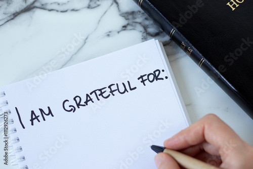 Open notebook with handwritten text for gratitude with holy bible book on white marble table. Top view. Thanksgiving to God Jesus Christ for blessings in diary.