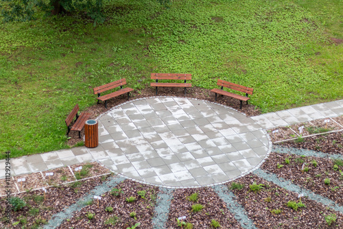 Fotografia A circular seating area with wooden benches surrounded by green grass and garden beds