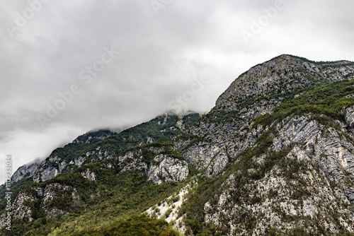 A rugged Slovenian mountain cloaked in mist, featuring dense greenery and rocky textures under an overcast sky