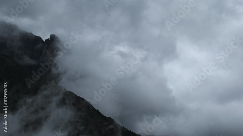 Time lapse of gray storm clouds blowing across a rocky mountain with distant trees
