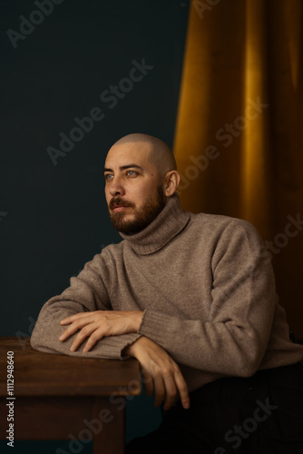 Portrait of a serious man sitting on a chair by a table in a studio.