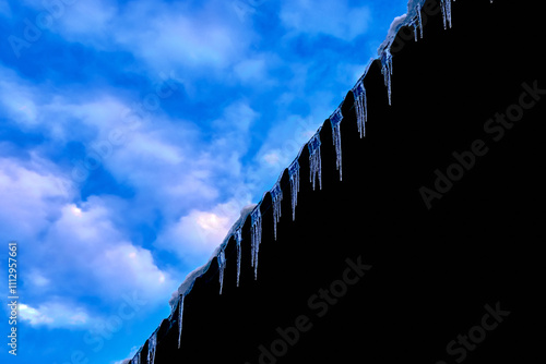 abstract blue sky with white clouds and icicles hanging on a black background reflecting the blue sky