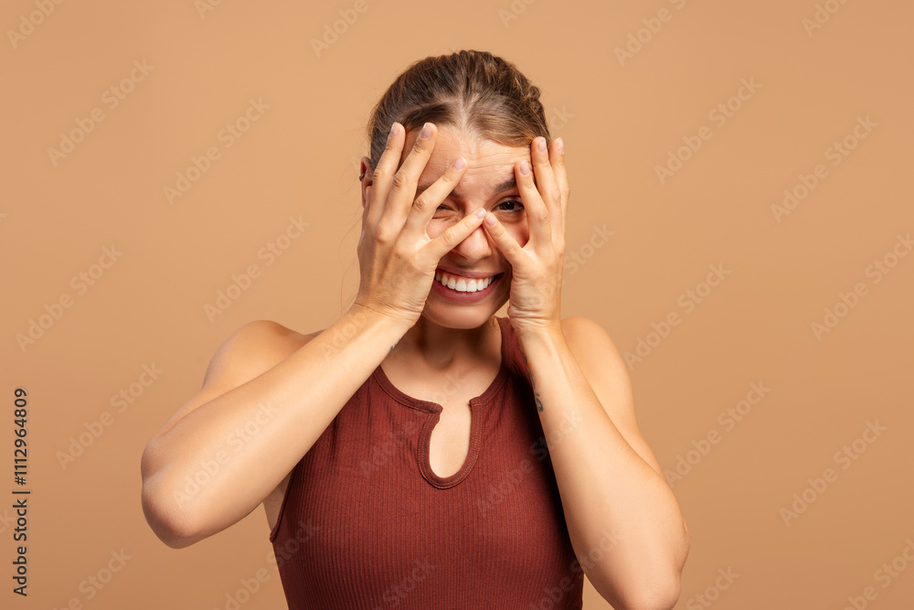 Young fit woman in sportwear hiding by hands looking at camera, isolated on beige Young fit woman in sportwear hiding by hands looking at camera, isolated on beige
