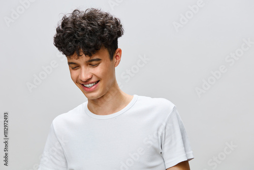 Wallpaper Mural Happy young man smiling casually in a plain white t shirt, with curly hair, against a soft gray background The image conveys a sense of joy and carefree attitude, perfect for lifestyle themes Torontodigital.ca