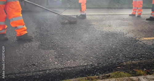 Road workers rake freshly laid hot asphalt tarmacadam