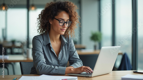 Focused Professional Woman Working on a Laptop in a Bright, Modern Office Setting