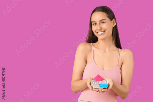 Young woman with condoms and contraceptive pills on purple background