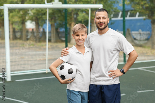 Father and his son with ball on soccer pitch