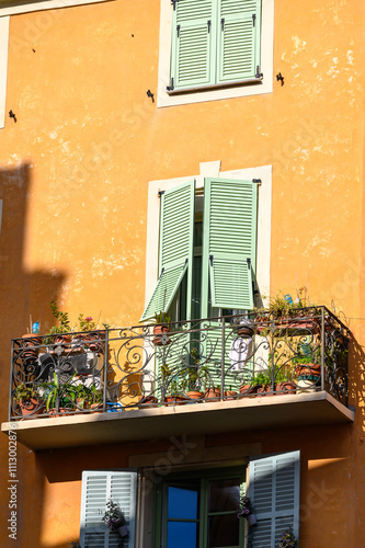 Fensterfassade mit Fensterläden und Pflanzen an einem Balkonfenster in Nizza, Côte d'Azur, Frankreich