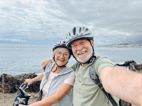 Two happy old mature people enjoying and riding bikes together to be fit and healthy outdoors. Active seniors having fun taking a selfie picture with camera