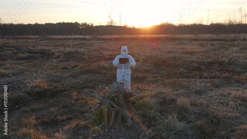 Foto Scientist in protective suit on devastated outdoor area with mask and tablet col