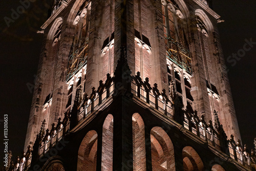 Architectural detail of renovated cathedral church tower of De Dom in Dutch diocese city lit up by newly installed lights in the darkness of night time photo